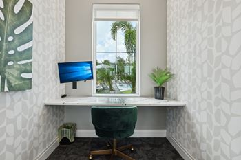 A white desk with a green chair and a blue monitor in front of a window.